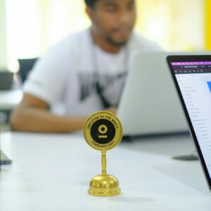 A man sitting at a desk with a laptop and a gold trophy