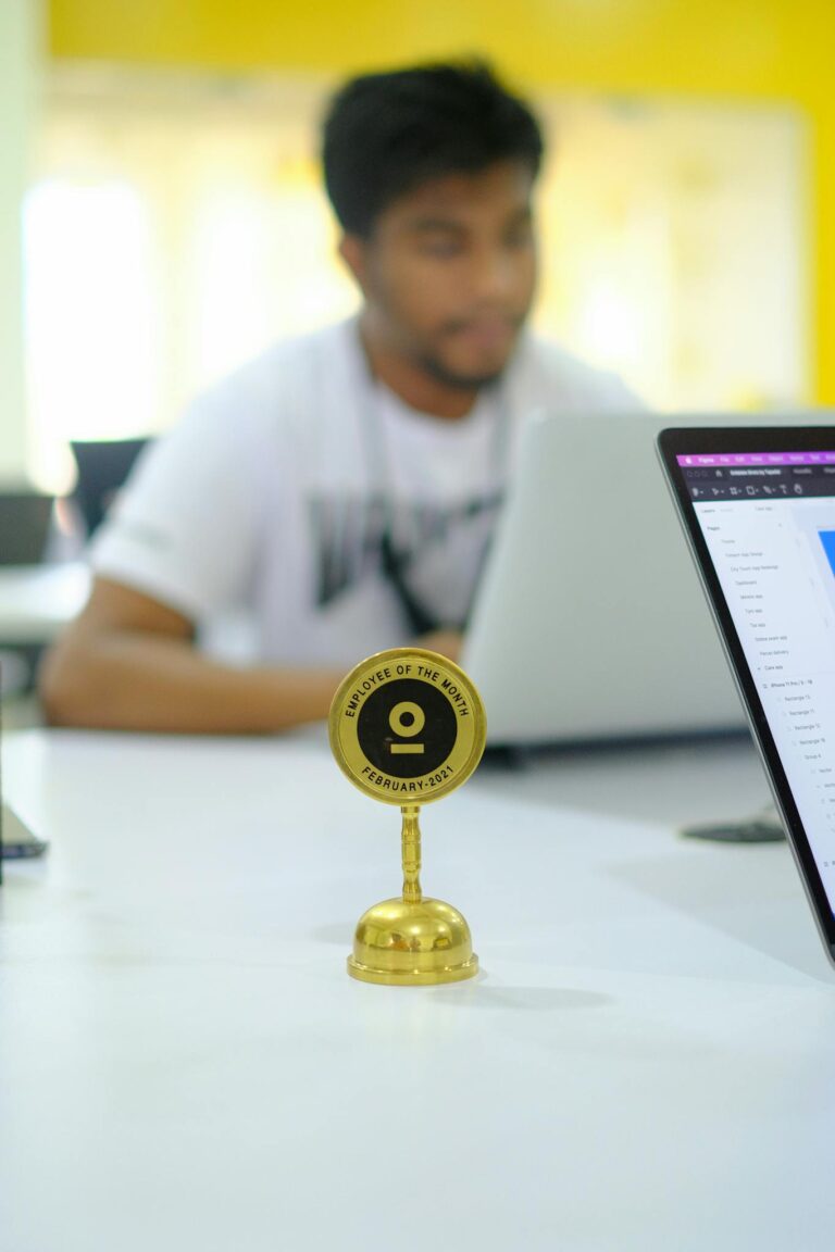 A man sitting at a desk with a laptop and a gold trophy